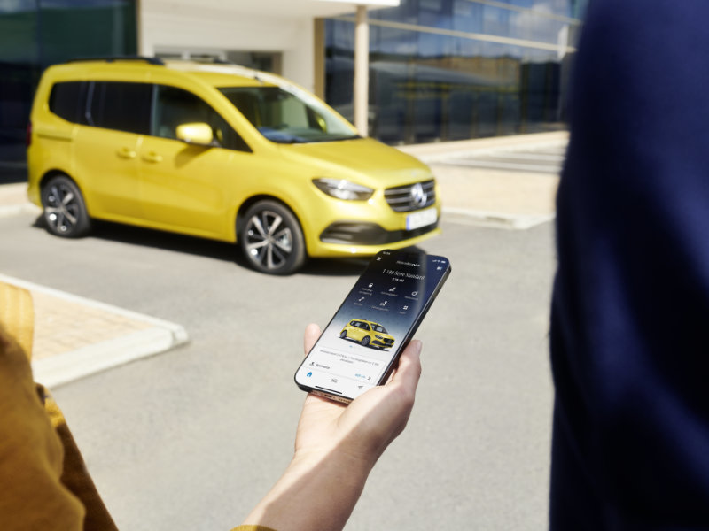 Mercedes-Benz me App auf Handy, T-Klasse im Hintergrund